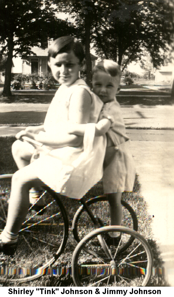 Black and white photo of Shirley 'Tink' Johnson sitting on a tricycle with Jimmy Johnson standing on the rear axle.